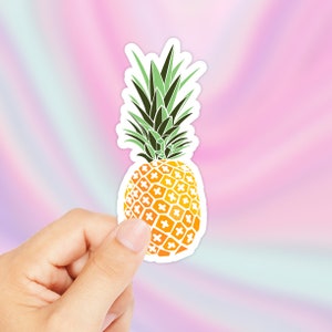 Op de afbeelding: Een gele ananas sticker met een wit en groen patroon. De sticker is op een roze en blauwe achtergrond.