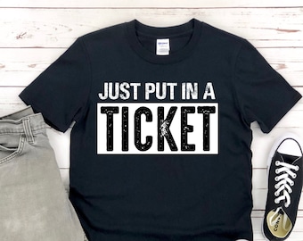May include: A black t-shirt with a white graphic that says "JUST PUT IN A TICKET" in a distressed font.