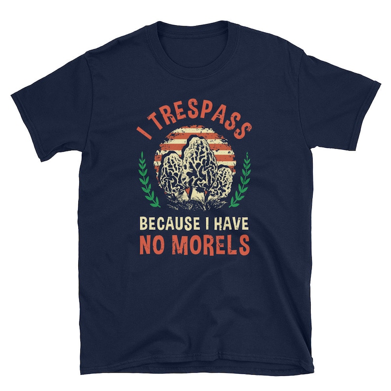 Pu&ograve; includere: T-shirt blu navy con una grafica di funghi spugnole e la scritta "I TRESSPASS BECAUSE I HAVE NO MORELS". Il design include un cerchio a strisce rosse e bianche e dettagli verdi.