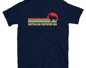 May include: A navy blue t-shirt with a retro-style sunset graphic featuring a silhouette of an Australian Shepherd dog. The text "AUSTRALIAN SHEPHERD DAD" is printed below the graphic.