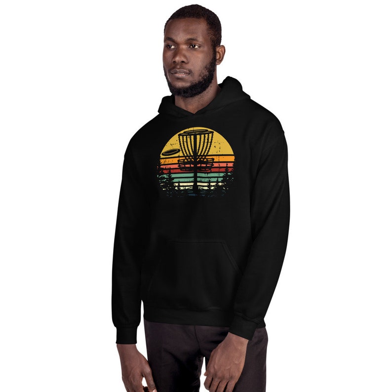 May include: Black hoodie with a vintage-style graphic of a disc golf basket and a disc flying through the air. The graphic is set against a sunset background with a yellow, orange, red, and blue color scheme.