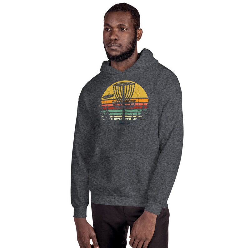 May include: A dark gray hoodie with a vintage-style graphic of a disc golf basket and disc in front of a sunset. The graphic is in shades of yellow, orange, red, and green.