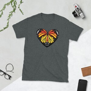 Puede incluir: Una camiseta gris oscuro jaspeada con un gr&aacute;fico de mariposa en forma de coraz&oacute;n. La mariposa tiene alas naranjas, amarillas y negras.