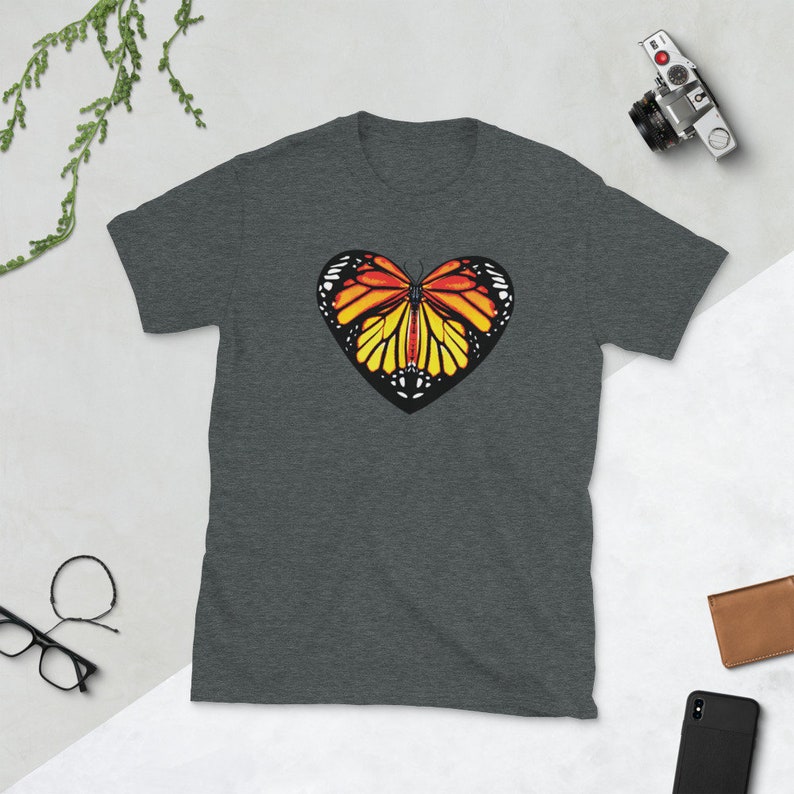 Puede incluir: Una camiseta gris oscuro jaspeada con un gr&aacute;fico de mariposa en forma de coraz&oacute;n. La mariposa tiene alas naranjas, amarillas y negras.