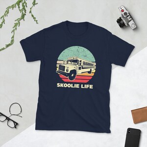 May include: A navy blue t-shirt with a vintage-style graphic of a yellow school bus driving through a sunset. The text "SKOOLIE LIFE" is printed below the graphic.