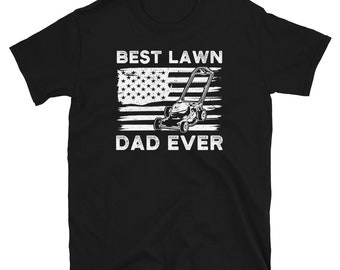 Puede incluir: Camiseta negra con un gráfico blanco de una cortadora de césped cortando una bandera estadounidense con el texto "Best Lawn Dad Ever".