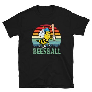 May include: Black t-shirt with a retro-style illustration of a bee wearing a baseball cap and holding a bat. The bee is in front of a sunset-colored circle with the text "BEESBALL" below.