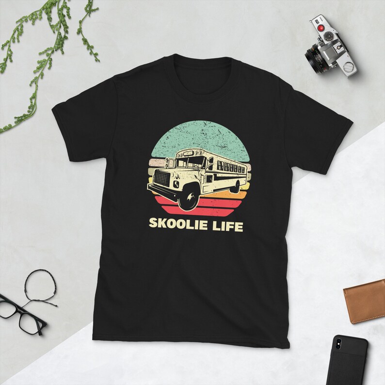 May include: Black t-shirt with a vintage-style graphic of a yellow school bus driving through a sunset. The text "SKOOLIE LIFE" is printed below the bus.