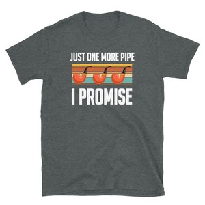 May include: A dark heather grey t-shirt with the text "Just one more pipe I promise" in white. The text is in a retro style with three red and black pipes.
