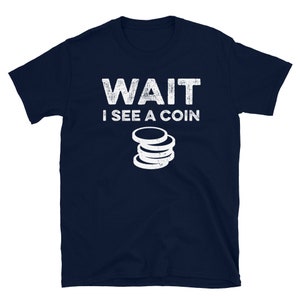 May include: A navy blue t-shirt with white text that reads "WAIT I SEE A COIN" and a stack of coins graphic.