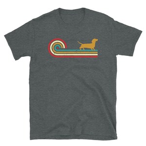 K&ouml;nnte beinhalten: Ein dunkel-melierter grauer T-Shirt mit einem Retro-Design, das eine Dackel-Silhouette vor einer mehrfarbigen gestreiften Welle zeigt.