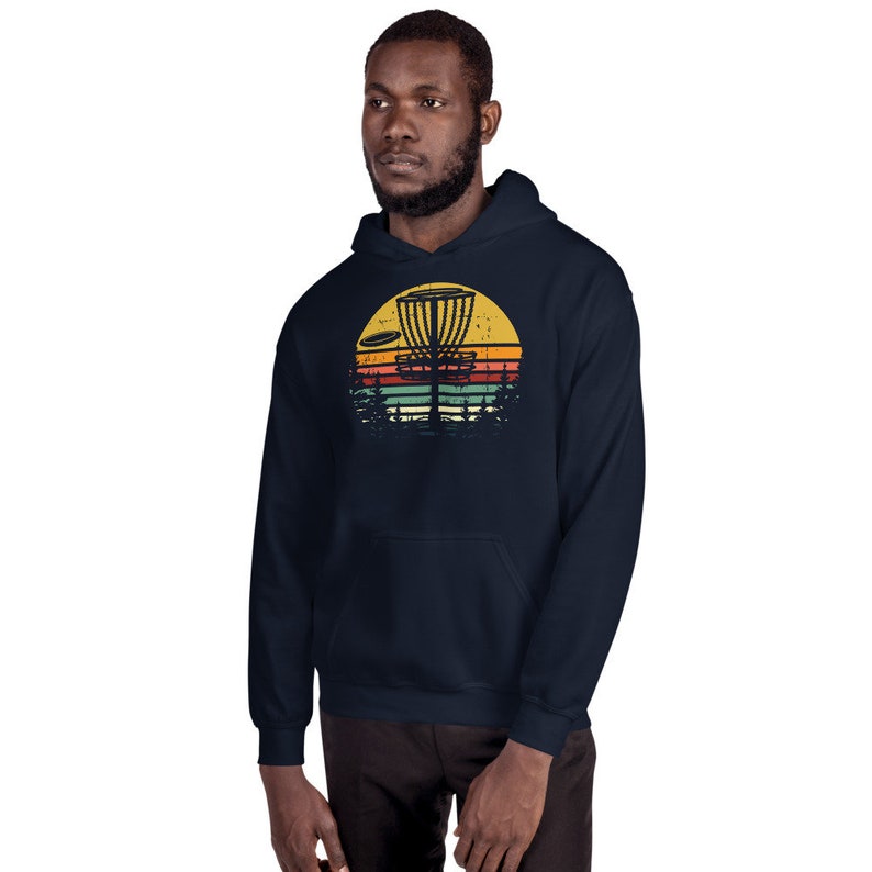 May include: A navy blue hoodie with a vintage-style graphic of a disc golf basket and a disc flying through the air. The graphic is set against a sunset background with orange, yellow, red, and blue stripes.