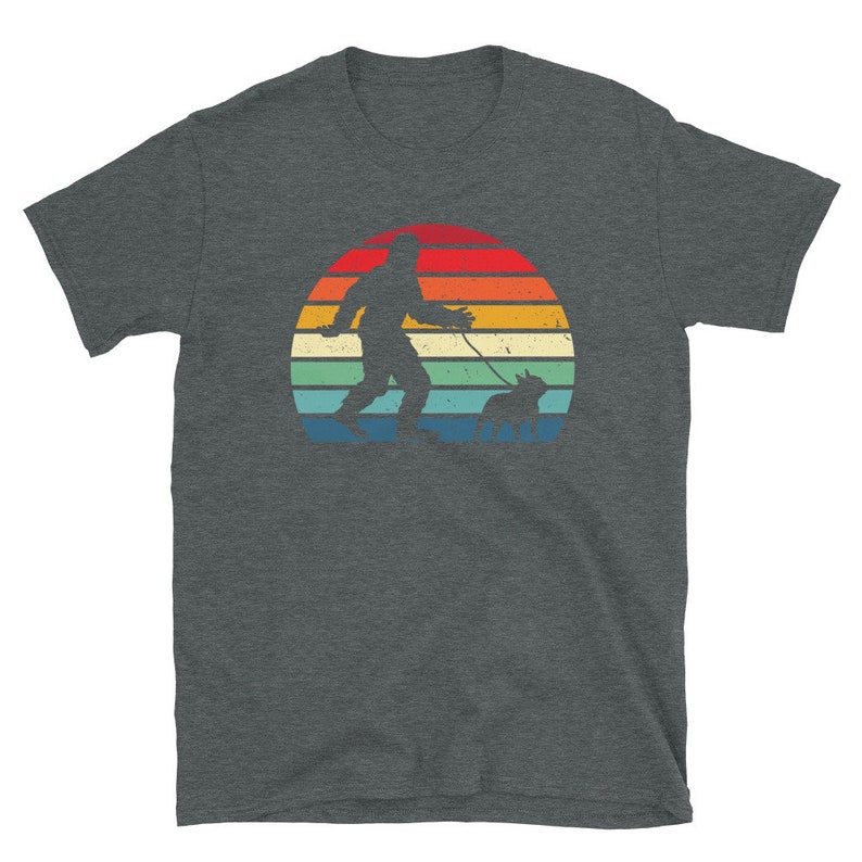 K&ouml;nnte beinhalten: Ein dunkel-helles graues T-Shirt mit einer Retro-Sonnenuntergangsgrafik, die eine Silhouette von Bigfoot zeigt, der einen Hund spazieren f&uuml;hrt.
