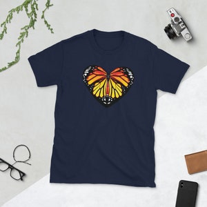 Puede incluir: Camiseta azul marino con un gr&aacute;fico de mariposa en forma de coraz&oacute;n. La mariposa tiene alas naranjas, amarillas y negras.