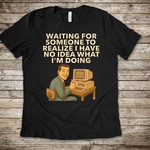 Pode incluir: T-shirt preto com o texto "WAITING FOR SOMEONE TO REALISE I HAVE NO IDEA WHAT I'M DOING." Uma ilustração retro mostra um homem de fato verde em frente a um computador, com o polegar para cima.