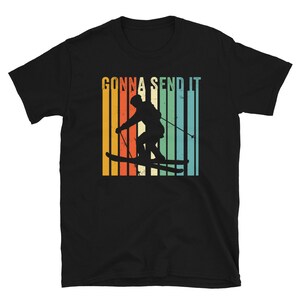 May include: Black t-shirt with a retro-style graphic of a skier in a colorful striped background. The text "Gonna Send It" is printed above the skier.
