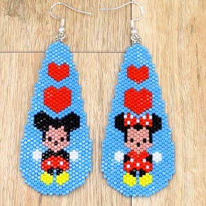 May include: A pair of beaded earrings featuring Mickey and Minnie Mouse. The earrings are teardrop-shaped with a light blue background, red hearts, and the characters in their classic outfits. The earrings have silver-coloured hooks.