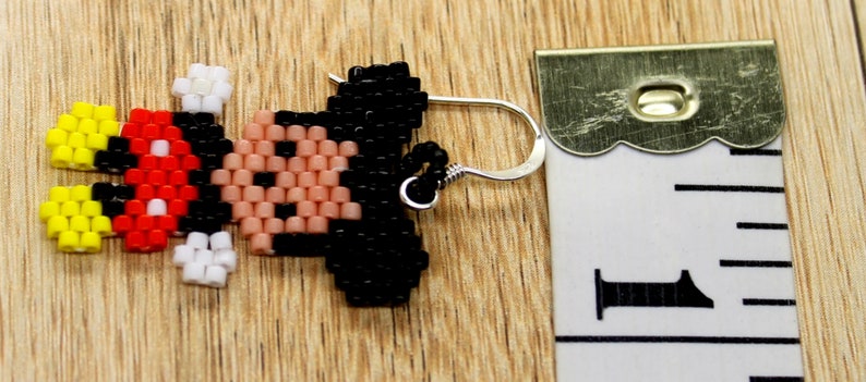 Peut inclure: Une paire de boucles d'oreilles en perles repr&eacute;sentant un Mickey Mouse en pixels. Les boucles d'oreilles sont rouges, noires, jaunes et blanches. Les boucles d'oreilles mesurent environ 2,5 cm de long et ont des crochets argent&eacute;s.