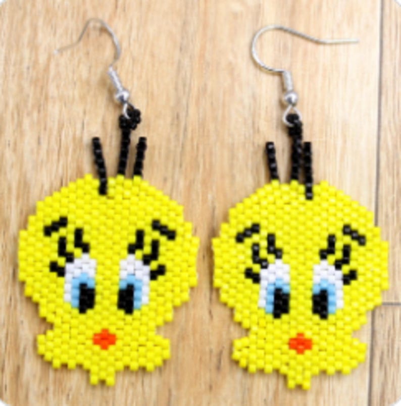 May include: A pair of yellow beaded earrings with a cartoon character design. The earrings have black accents, blue eyes, and a red mouth. They hang from silver-coloured fish hook ear wires.
