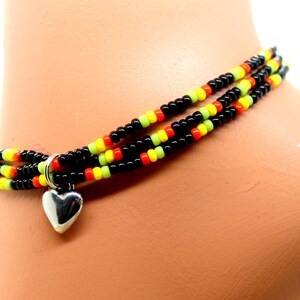 May include: Multi-strand beaded anklet with black, yellow, orange and green beads. The anklet has a silver heart charm.