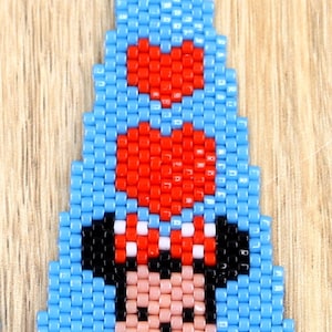 May include: A beaded earring with a cartoon character design. The earring is mainly blue, with red hearts and a character's face in the centre. The earring has a silver hook.