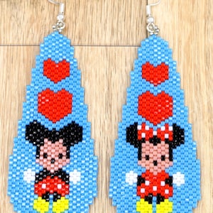 May include: A pair of beaded earrings featuring Mickey Mouse and Minnie Mouse. The earrings have a light blue background with red heart accents. Mickey Mouse is wearing red shorts and Minnie Mouse is wearing a red polka dot dress.