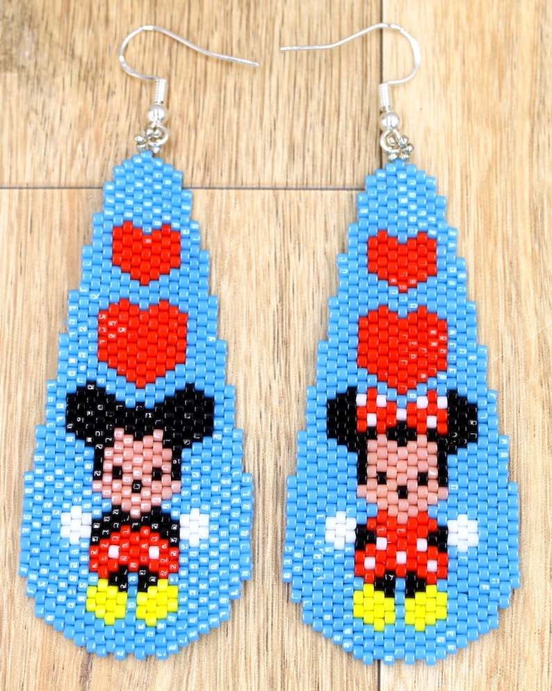 May include: A pair of beaded earrings featuring Mickey Mouse and Minnie Mouse. The earrings have a light blue background with red heart accents. Mickey Mouse is wearing red shorts and Minnie Mouse is wearing a red polka dot dress.