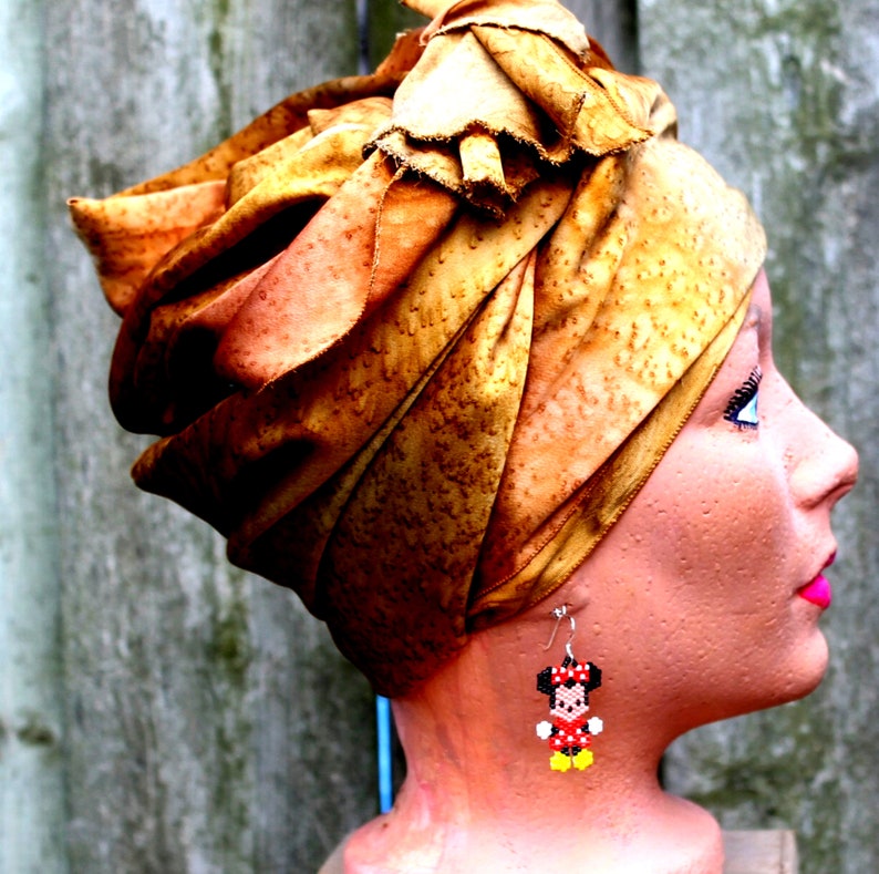 Peut inclure: Une t&ecirc;te de mannequin portant un turban couleur rouille avec une boucle d'oreille Minnie Mouse en perles. La boucle d'oreille est rouge, noire et jaune.