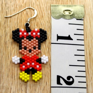 Peut inclure: Une paire de boucles d'oreilles en perles avec un motif pixelis&eacute; de Minnie Mouse. Les boucles d'oreilles sont rouges, noires, blanches et jaunes. Les boucles d'oreilles mesurent environ 2,5 cm de long.
