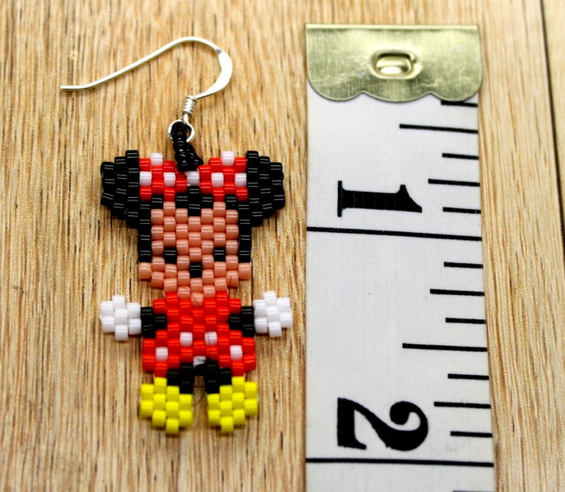 Peut inclure: Une paire de boucles d'oreilles en perles avec un motif pixelis&eacute; de Minnie Mouse. Les boucles d'oreilles sont rouges, noires, blanches et jaunes. Les boucles d'oreilles mesurent environ 2,5 cm de long.