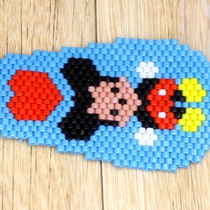 May include: A beaded earring with a Mickey Mouse design. The earring is mainly light blue with red, black, pink, and yellow details. The earring is approximately 2.5 cm long.