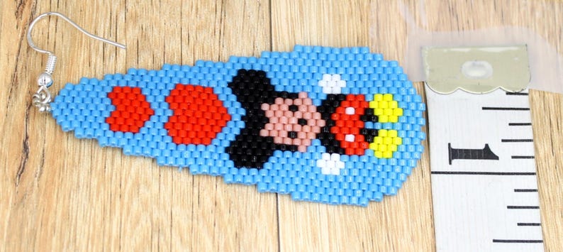 May include: A beaded earring with a Mickey Mouse design. The earring is mainly light blue with red, black, pink, and yellow details. The earring is approximately 2.5 cm long.