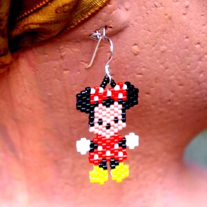 Peut inclure: Une paire de boucles d'oreilles en perles repr&eacute;sentant un personnage de dessin anim&eacute; avec une robe rouge, des chaussures noires et un n&oelig;ud noir. Le personnage est une souris de dessin anim&eacute; populaire.