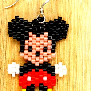 Peut inclure: Boucles d'oreilles Mickey Mouse en perles avec des cheveux noirs, une peau rose, un short rouge, des gants blancs et des chaussures jaunes.