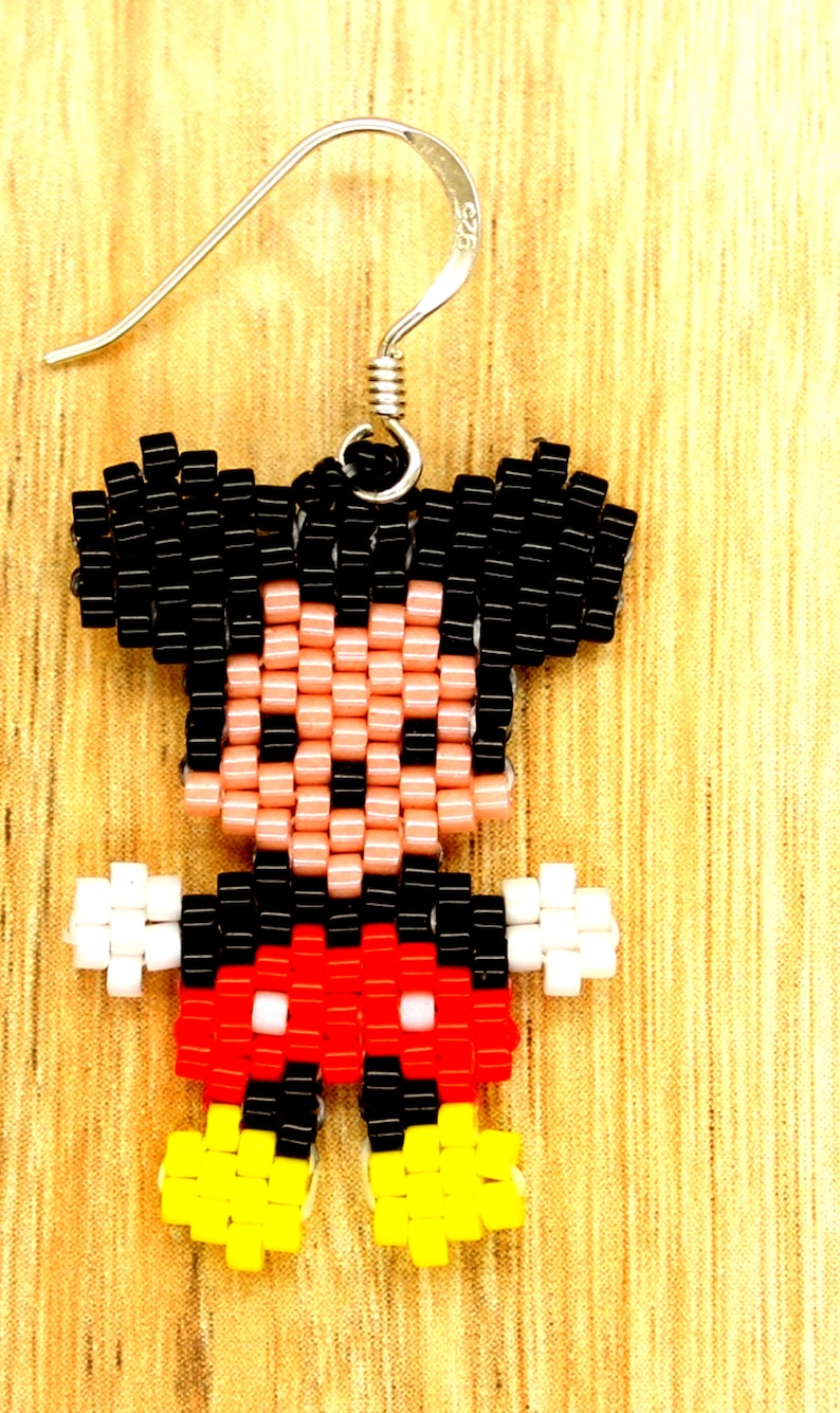 Peut inclure: Boucles d'oreilles Mickey Mouse en perles avec des cheveux noirs, une peau rose, un short rouge, des gants blancs et des chaussures jaunes.