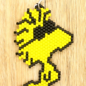 May include: Yellow and black beaded earring shaped like a cartoon bird. The earring is made of small beads and has a silver hook.