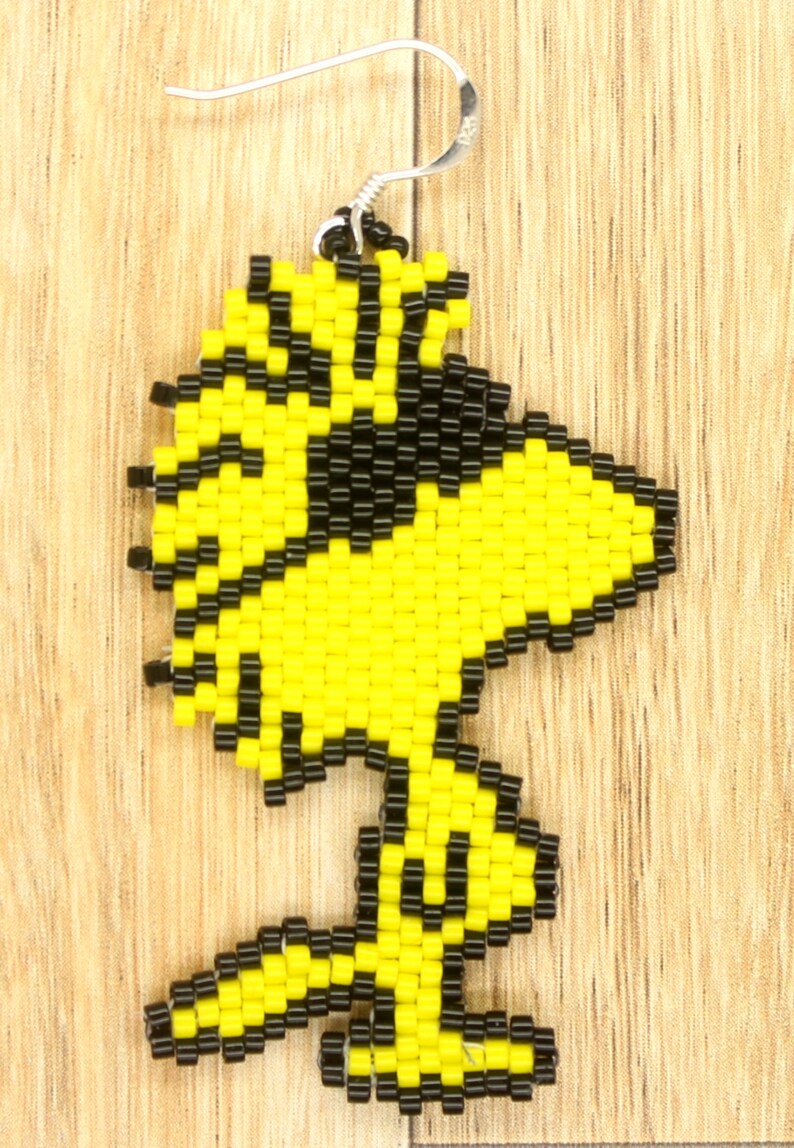 May include: Yellow and black beaded earring shaped like a cartoon bird. The earring is made of small beads and has a silver hook.