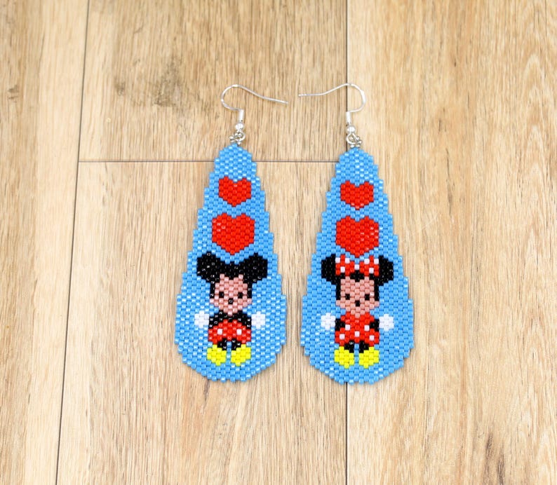 May include: A pair of beaded earrings featuring Mickey and Minnie Mouse. The earrings are teardrop-shaped with a light blue background, red hearts, and the characters in their classic outfits. The earrings have silver-coloured hooks.