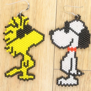 May include: A pair of beaded earrings featuring cartoon characters. One earring is yellow and black and depicts a bird with a beak. The other earring is white and black and depicts a dog with a red collar.