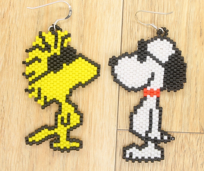 May include: A pair of beaded earrings featuring cartoon characters. One earring is yellow and black and depicts a bird with a beak. The other earring is white and black and depicts a dog with a red collar.