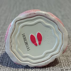 May include: A small, round, pink and white decorative item. The bottom is light gray with the text "&copy;Disney Just Play CHINA" and the number "1836LH01A1". Two red footprints are also visible.