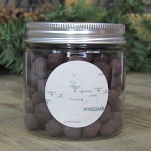 May include: A clear glass jar filled with dark brown chocolate candies. The jar has a silver lid and a white label with a map of the Mesabi Iron Range in Minnesota and the text "#MESABI".