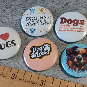 May include: A collection of six round dog-themed buttons. One button reads "I ♥ DOGS" with a red heart. Other buttons feature phrases like "DOG HAIR don't care" and "Dogs do talk." One button has a dog wearing sunglasses.