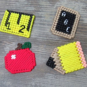 May include: Four felt crafts in the shape of a ruler, a chalkboard, an apple, and a pencil. The ruler is yellow with black numbers "1" and "2". The chalkboard is black with white letters "A", "B", and "C". The apple is red with a white highlight and a green stem. The pencil is yellow with a black eraser and a pink eraser.