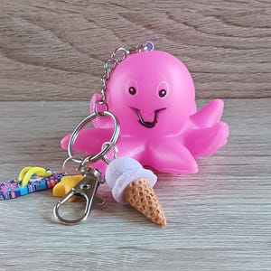 May include: A pink octopus keychain with a smiling face, attached to a silver chain with a lobster clasp. Additional charms include a miniature ice cream cone and a flip-flop. The keychain is a fun accessory.
