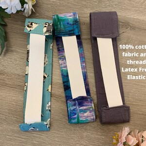 May include: Three headbands with different fabric patterns. The headband on the left has a blue and white pattern with small white dogs. The middle headband has a blue and purple watercolour pattern. The headband on the right is solid dark grey. All headbands have white elastic and are made with 100% cotton fabric and thread.  Latex Free Elastic.