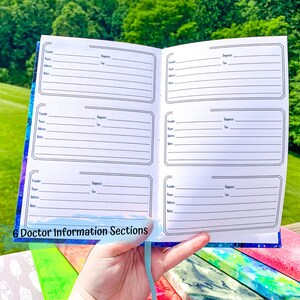 Peut inclure: Carnet ouvert avec six sections d'informations m&eacute;dicales. Chaque section comprend des champs pour le fournisseur, le nom, l'adresse, le t&eacute;l&eacute;phone, le fax, le diagnostic et les notes. Le carnet a une couverture sur le th&egrave;me de la galaxie bleue et violette et un ruban bleu clair.