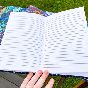 May include: An open lined notebook with a blue and purple patterned cover. The notebook is lying on a wooden surface.