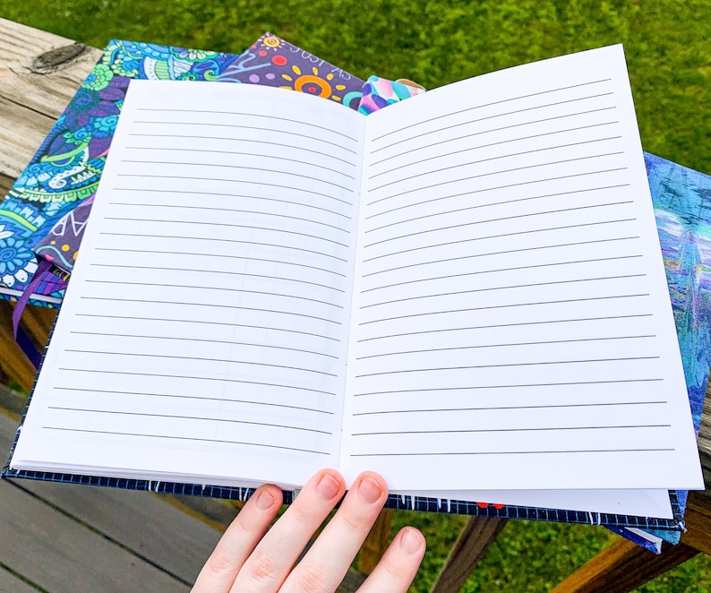 May include: An open lined notebook with a blue and purple patterned cover. The notebook is lying on a wooden surface.