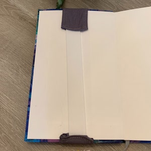 May include: A blue and purple patterned notebook with a white elastic closure and a grey fabric bookmark.